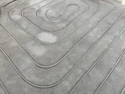 Wykonane frezowanie pod ogrzewanie podłogowe. Rury ułożone w betonowej posadzce tworzą spiralny wzór, gotowe do zalania.
