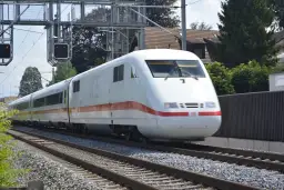 Biały pociąg ICE z czerwonym pasem jedzie po torach. Czy TLK to Intercity? Nie, to niemiecki pociąg dużych prędkości.