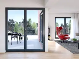 Nowoczesne okna antracytowe z widokiem na taras i ogród. W salonie czerwony fotel i kominek.