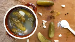 Garnki z ogórkami kiszonymi, czosnkiem, koprem i solą na drewnianym tle.