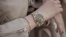 Damski zegarek na złotej bransolecie z ciemną tarczą, noszony na nadgarstku.