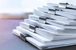 Stos dokumentów z klamrami. Zastanawiasz się, jakie dokumenty są potrzebne do sprzedaży działki rolnej? Oto stos papierów, które mogą być kluczowe.