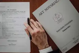 Dłoń z obrączką trzyma długopis nad dokumentem "Akt Notarialny". Zastanawiasz się, ile kosztuje poświadczenie podpisu u notariusza?