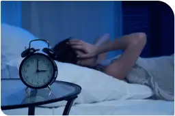 Budzik pokazuje 3:00. Osoba w łóżku, z rękami na głowie, cierpi na bezsenność po MSM.