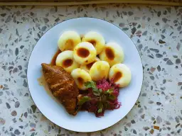 Talerz z kluskami śląskimi, roladą i czerwoną kapustą.