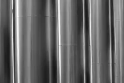 Pionowe, metalowe rury tworzą abstrakcyjną kompozycję. Czy stal nierdzewna przewodzi prąd? To pytanie nasuwa się, patrząc na te gładkie, odbijające światło powierzchnie.