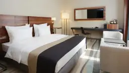 Nowoczesne wyposażenie pokoi hotelowych: wygodne łóżko, biurko z TV, fotele i stolik.