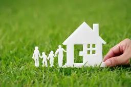 Biała rodzina z papieru i dom na trawie. Dłoń odłącza dom, symbolizując odłączenie się od wspólnoty mieszkaniowej.