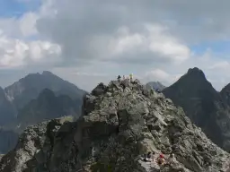 Grupa turystów odpoczywa na skalistym szczycie, podziwiając widok na Tatry. Trasa na Rysy jest wymagająca, ale widoki wynagradzają wysiłek.
