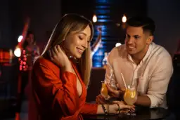 Uśmiechnięta kobieta w czerwonej sukience i mężczyzna przy drinkach. Czy to jej triki działające na mężczyzn?