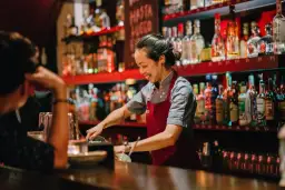 Uśmiechnięta barmanka w Gdańsku przygotowuje drinka. Zastanawiasz się, ile zarabia barman w Gdańsku?