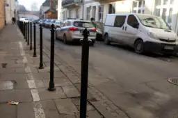 Słupek chodnikowy, radiowóz i biały van na ulicy.