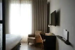Przytulny pokój hotelowy z wygodnym łóżkiem, fotelem i biurkiem. Zastanawiasz się, ile kosztuje nocleg w takim miejscu?