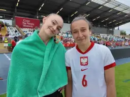 Dwie młode piłkarki w strojach reprezentacji Polski na tle trybun stadionu.