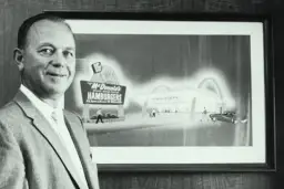 Ray Kroc, który wymyślił McDonald's, stoi obok obrazu przedstawiającego pierwszy lokal.