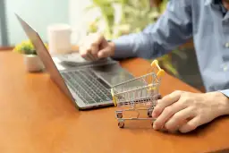 Osoba przy laptopie z małym wózkiem sklepowym uczy się, jak założyć sklep na WordPress.