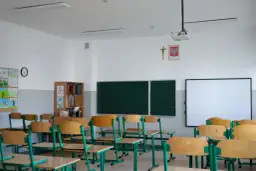 Pusta klasa szkolna z rzędami ławek, tablicą i projektorem.
