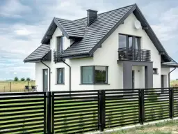 Nowoczesny dom z białymi ścianami i czarnym dachem. Eleganckie wykończenie ściany szczytowej podkreśla jego architekturę.