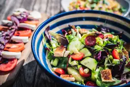 Kolorowa sałatka z pomidorkami, ogórkiem i grzankami, idealna na dietę low carb. Obok caprese.