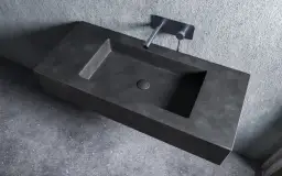 Nowoczesna umywalka z betonu o minimalistycznym designie, z wpuszczonym w blat odpływem i elegancką baterią ścienną.