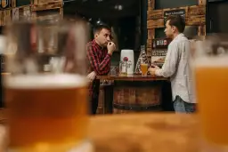 Dwóch mężczyzn rozmawia przy barze z piwem, w tle dekoracje związane z piwem.