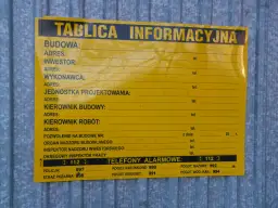 Tablica informacyjna na budowie. Widać pola na dane inwestora, kierownika budowy, numer pozwolenia na budowę i telefony alarmowe. Ważne jest pozwolenie na budowę, by wszystko było legalne.