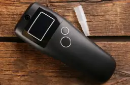 Czarny alkomat z wyświetlaczem i ustnikiem na drewnianym tle. Gdzie kupić alkomaty?