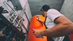 Instalator sprawdza termometr na pomarańczowym bojlerze. Dowiedz się, ile kosztuje piec gazowy do centralnego ogrzewania.