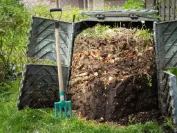 Przydomowy kompostownik pełen resztek organicznych, obok widły. To miejsce, gdzie powstaje cenny nawóz, a nie tylko odpady.