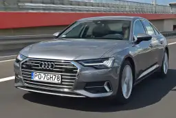 Szary sedan Audi A6 jedzie po drodze, widoczny przód i bok.