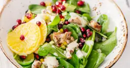 Sałatka ze szpinakiem, kurczakiem, pomarańczą i granatem. Duża ilość sałaty w misce, z dodatkami.