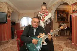 Uśmiechnięty mężczyzna gra na gitarze, a za nim stoi kobieta. Nie wiadomo, ile lat ma Don Vasyl, ale wygląda na szczęśliwego.