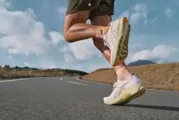 Biegacz w lekkich, białych butach do maratonu pokonuje krętą drogę na tle górskiego krajobrazu.
