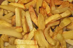 Złociste frytki smażące się na głębokim oleju na patelni.