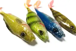 Cztery gumowe przynęty wędkarskie w kształcie rybek w różnych kolorach.