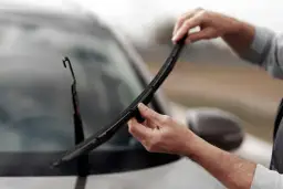 Dłonie mężczyzny wymieniające pióro wycieraczki samochodowej na przedniej szybie.