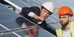 Dwóch inżynierów w kaskach analizuje panele słoneczne. Jeden z nich wskazuje coś na panelu, zastanawiając się, ile mocy 4mm2 może wygenerować.