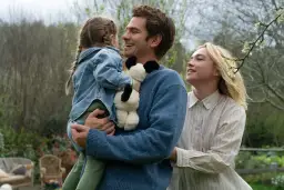 Szczęśliwa rodzina w ogrodzie. Ojciec trzyma córkę z pluszakiem, matka patrzy z uśmiechem. Czy to początek melodramatu?