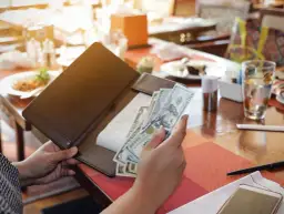 Rachunek w restauracji, ręka trzyma banknoty dolarowe. Poproszę rachunek po angielsku.