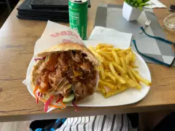 Kebab w bułce z frytkami na talerzu, obok puszka napoju.