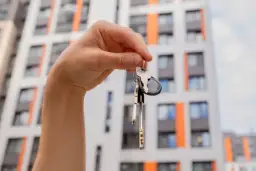 Dłoń trzymająca pęk kluczy na tle nowoczesnego bloku mieszkalnego.