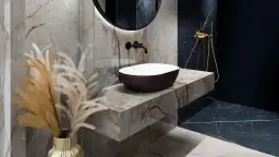 Elegancki blat pod umywalkę z płytek imitujących marmur, z umieszczoną na nim owalną umywalką i złotą armaturą.