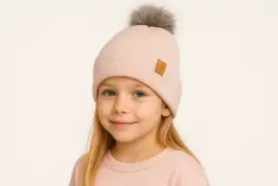 Uśmiechnięta dziewczynka w pudrowym komplecie z pomponem na czapce. Idealny komin dla dziecka na zimowe zabawy.