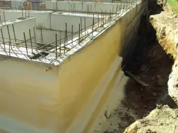 Zastosowano izolację pionową fundamentów. Widać zbrojenie i betonowe ściany fundamentowe, a obok wykop z ziemią.