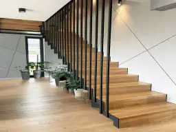 Nowoczesne drewniane schody z czarną balustradą. Zastanawiasz się, ile kosztuje zrobienie schodów? Warto rozważyć ten projekt.