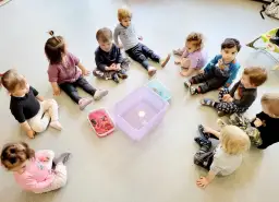 Dzieci siedzą w kółku na podłodze wokół pojemników z wodą i zabawkami.