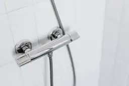 Chromowany panel prysznicowy na białej, kafelkowej ścianie. Idealny, gdy zastanawiasz się, jak zrobić prysznic na działce rekreacyjnej.