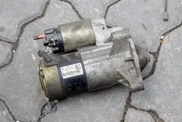 Rozrusznik samochodowy, kluczowy element do uruchomienia silnika. Widać jego metalową obudowę i złącza.