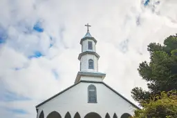 Biały kościół z krzyżem na wieży, pod błękitnym niebem. Planujesz ślub i zastanawiasz się, jak załatwić bierzmowanie przed ślubem?