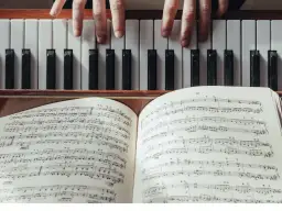 Dłonie grające na pianinie, przed nimi otwarta księga z nutami i tabelą akordów.